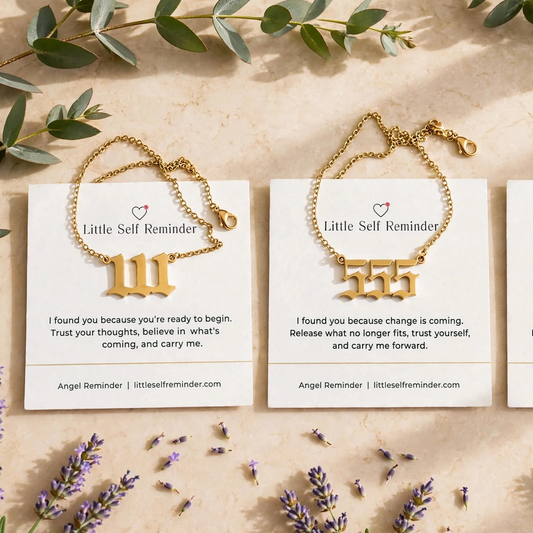 Three gold-toned reminder bracelets displayed on white cards, arranged in a flat lay with eucalyptus leaves and lavender sprigs on a light beige background.