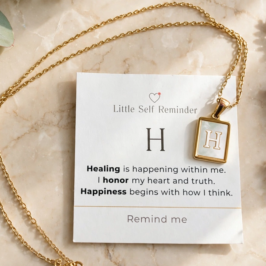 A gold necklace with a square pendant displayed on a white card that reads 'Little Self Reminder' with a motivational quote.