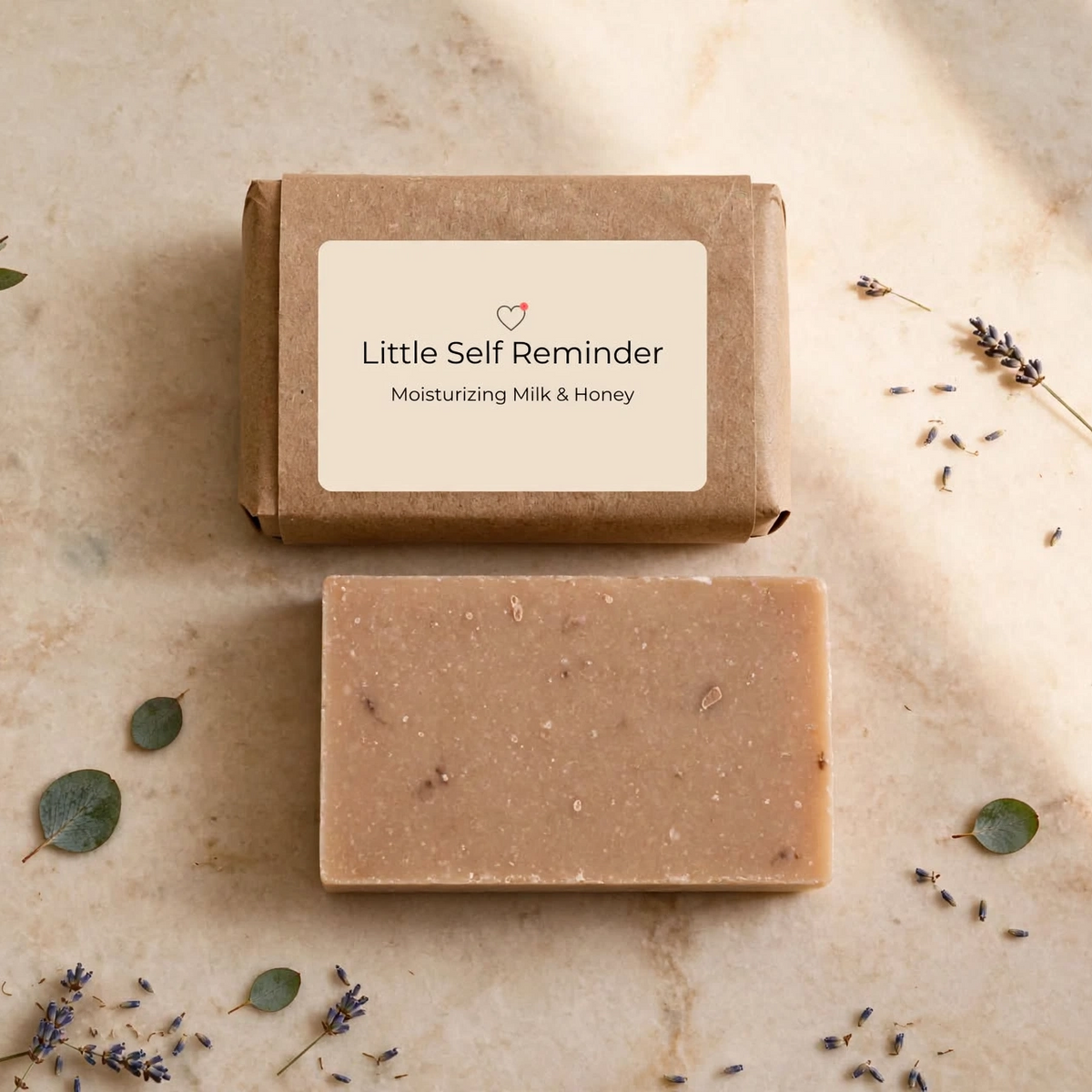 A rectangular bar of handmade soap in a natural tan color with visible botanical inclusions, displayed below its Kraft paper packaging box.
