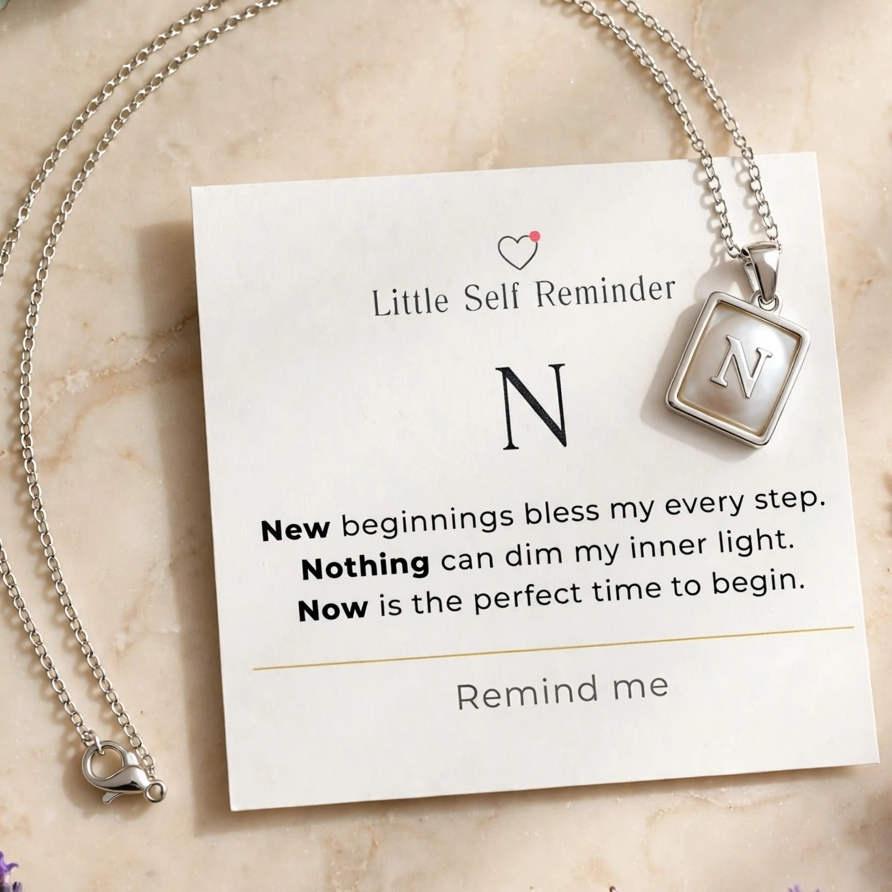 A silver necklace with a square pendant engraved with 'N' and 'Love', displayed on a white card that reads 'Little Sell Reminder' with a motivational quote.