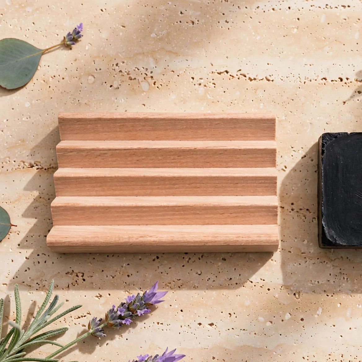 Two handmade rectangular soap bars sit on a textured beige stone surface with botanical props.