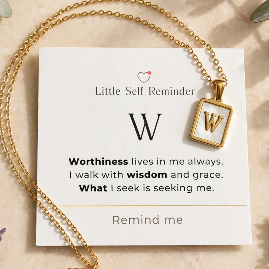 Gold necklace with a square pendant featuring the letter 'W' and a 'Little Self Reminder' card, styled in a flat lay with lavender and eucalyptus on a beige surface.