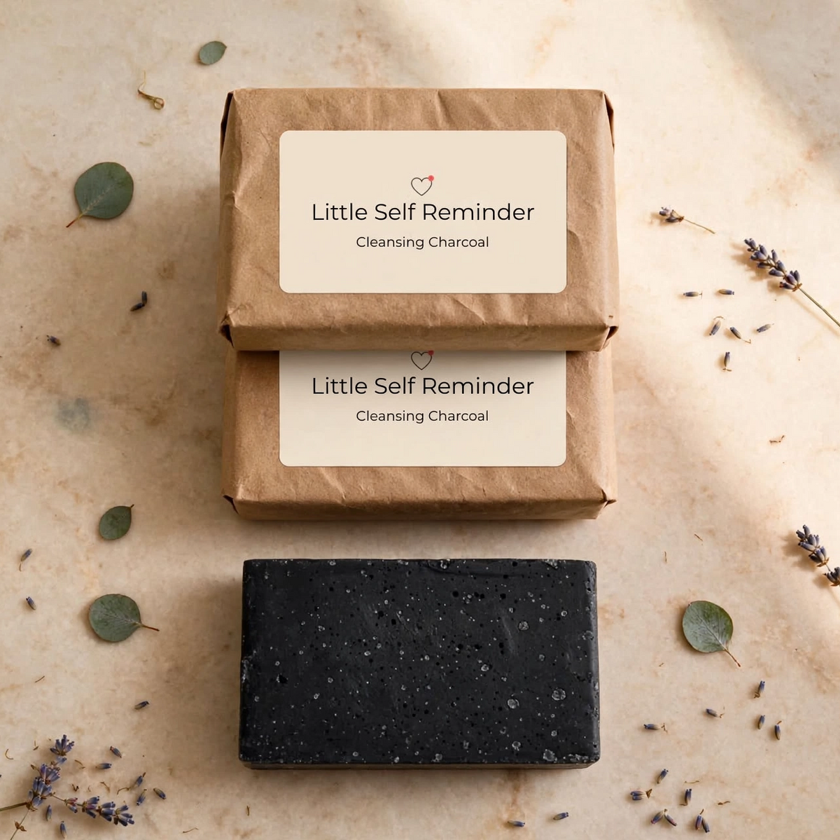 Two stacked brown Kraft paper boxes labeled 'Little Self Reminder Cleansing Charcoal' with a single dark charcoal rectangular bar of soap placed below.
