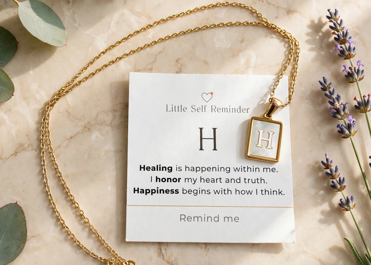 A gold necklace with a square pendant displayed on a white card that reads 'Little Self Reminder' with a motivational quote. 