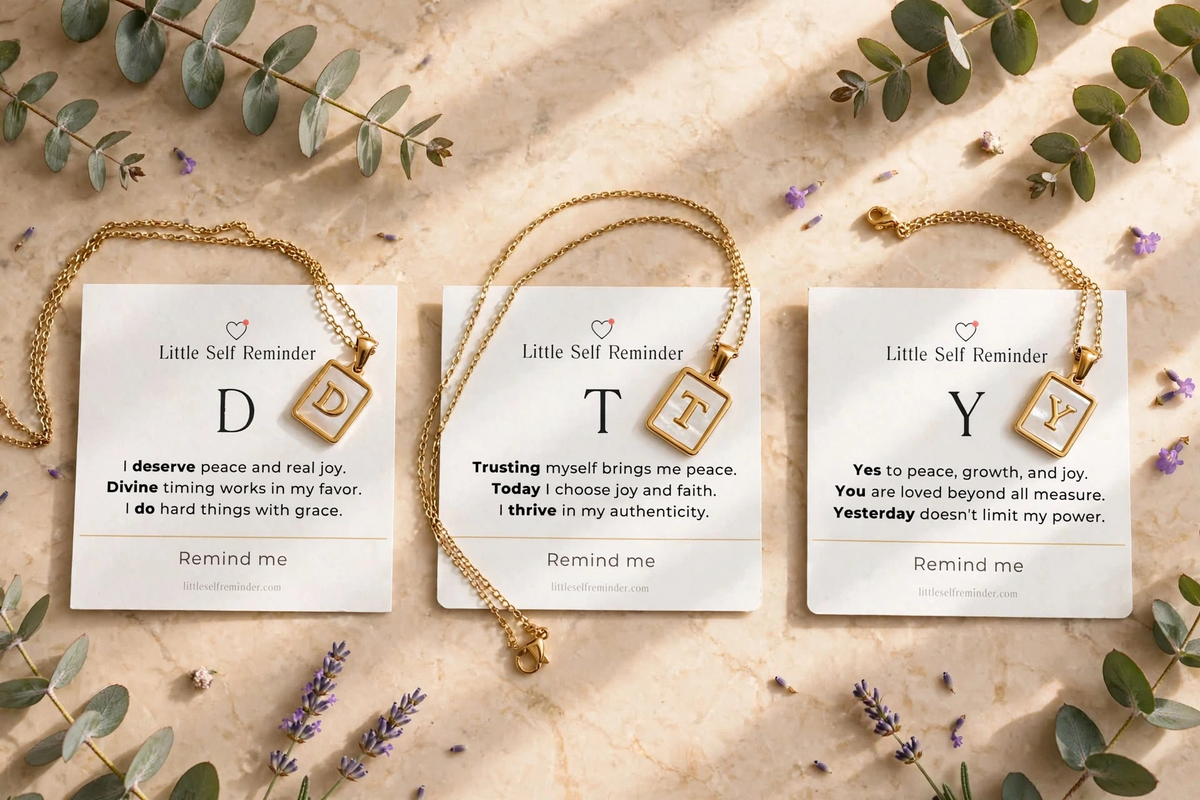 Gold-toned chain necklaces with square pendant cards displayed on a light beige marble surface. 