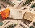 Three artisanal soap bars arranged on a textured beige surface with eucalyptus leaves and lavender sprigs.