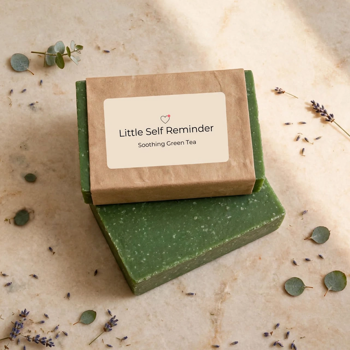 A stacked set of two green soap bars, one wrapped in brown Kraft paper with a cream label reading 'Little Self Reminder Soothing Green Tea'.