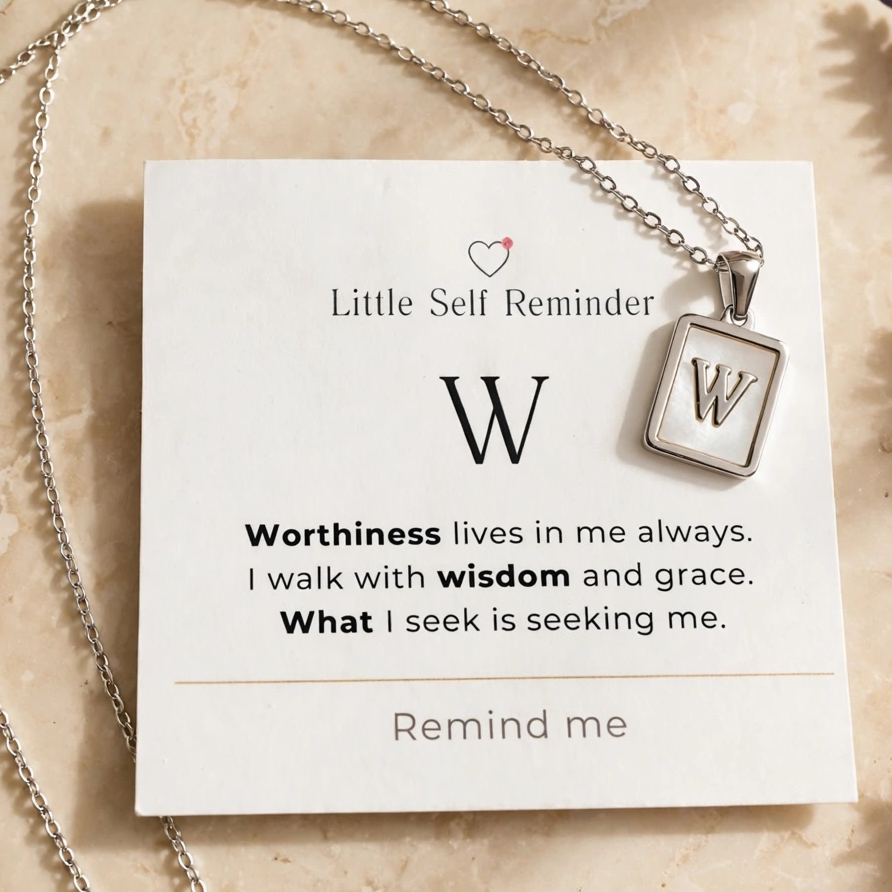 A silver necklace with a square pendant featuring the letter 'W' is displayed on a white card that reads 'Little Self Reminder' with a quote starting with 'W'.