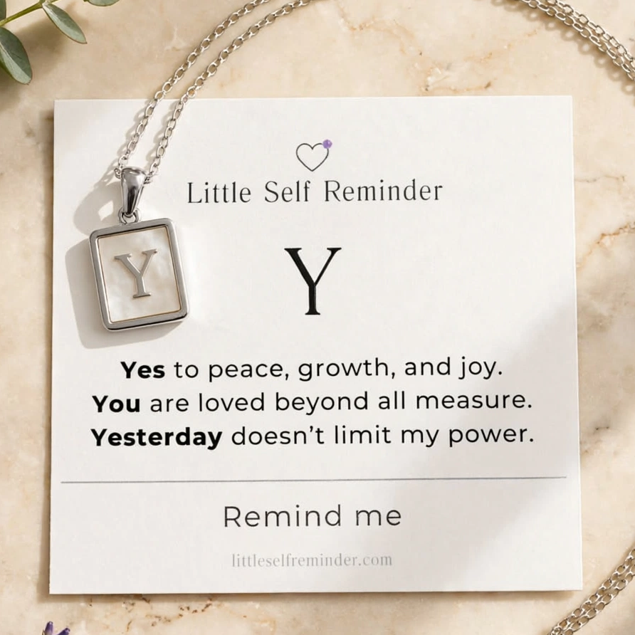 A silver necklace with a square pendant featuring the letter 'Y' is displayed on a white card that reads 'Little Self Reminder' with a positive affirmation.