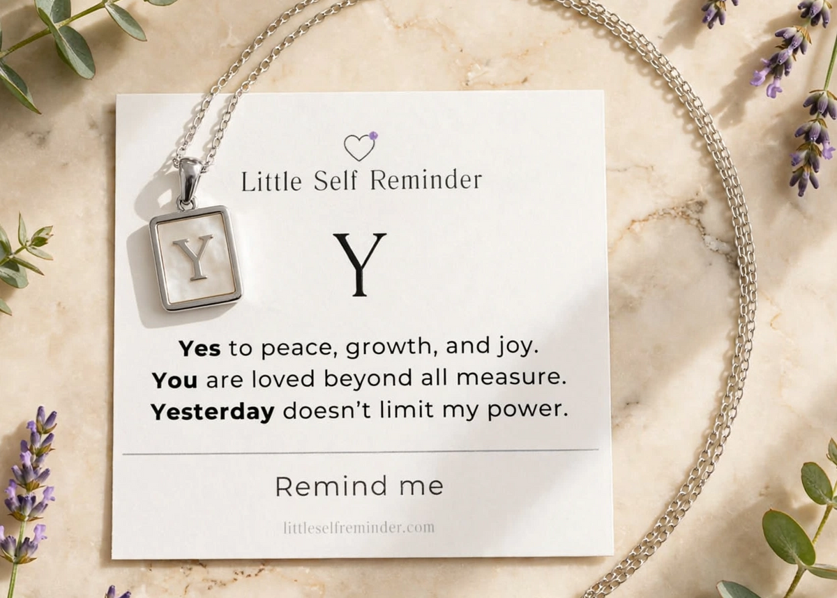 A silver necklace with a square pendant featuring the letter 'Y' is displayed on a white card that reads 'Little Self Reminder' with a positive affirmation.